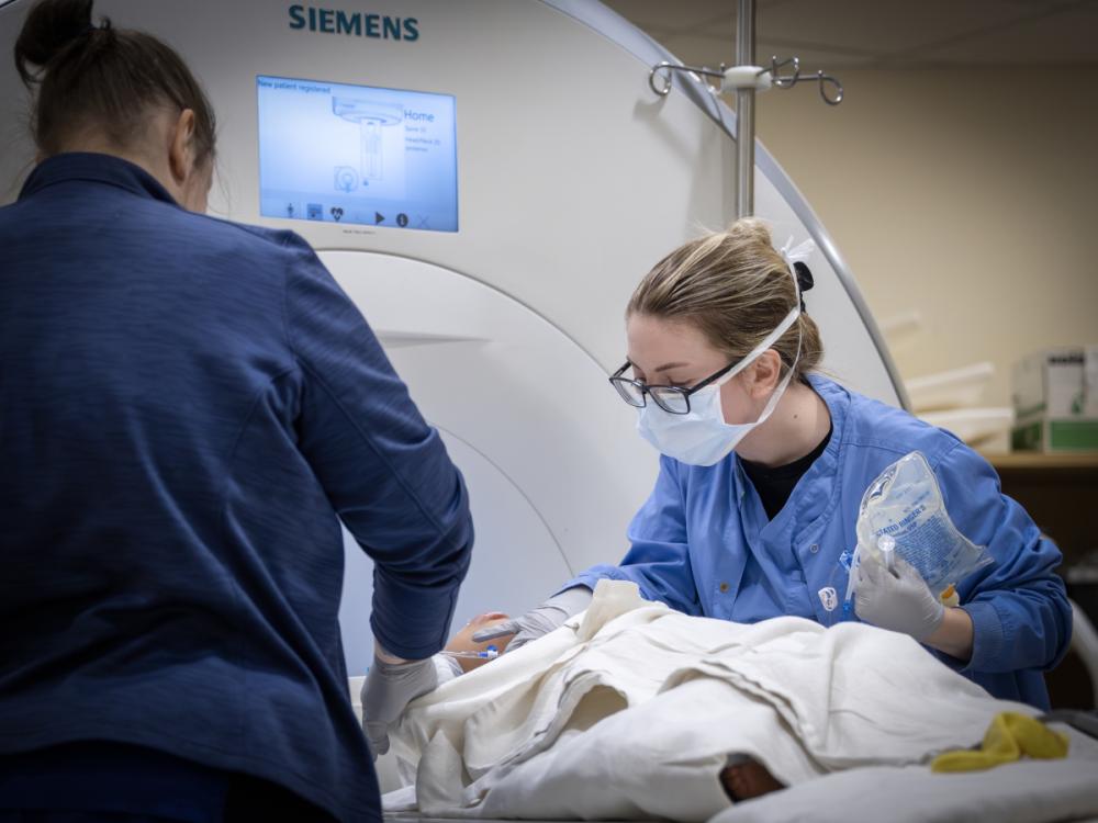 Two clinical team members tend to a patient who lays on a table of an MRI machine.
