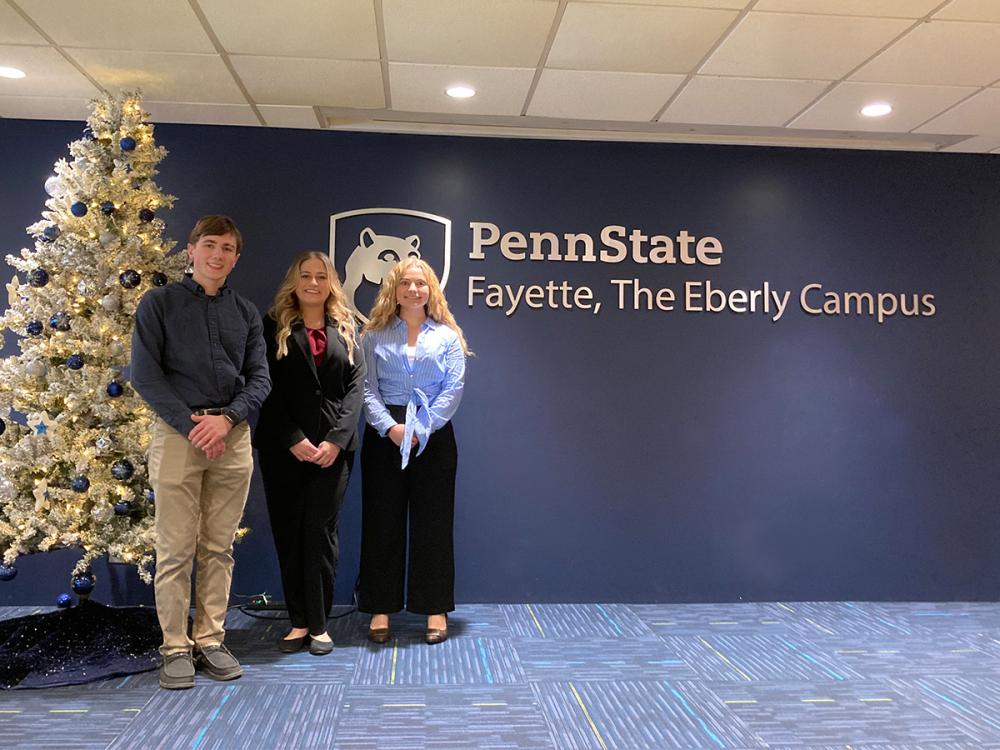 Joseph Kirsch, Morgan Amoroso, and Sidney Bergman pose in front of the Penn State Fayette, The Eberly Campus sign inside the Student Success Center.