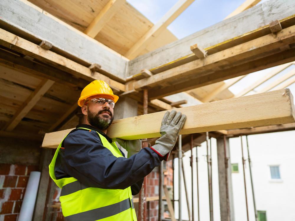 A roofer carrying timber at a construction site.