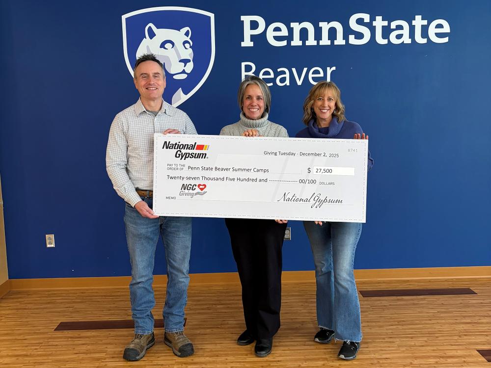 A photo of a man and two women holding a giant check in front of a Penn State Beaver wall