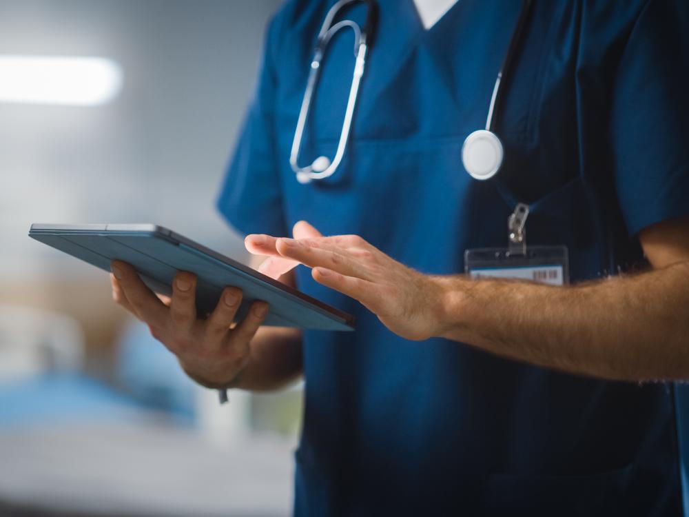 Medical professional's mid-section with a stethoscope around neck typing on iPad.
