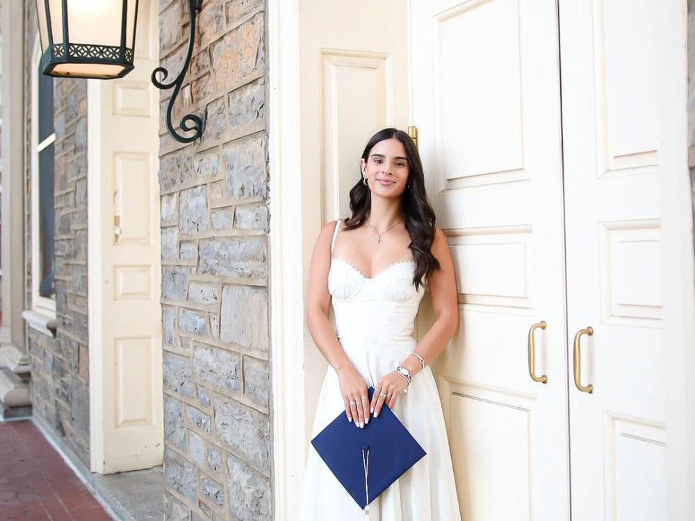 Kayla Lynch holds a graduation cap while standing outside Old Main in a white dress.