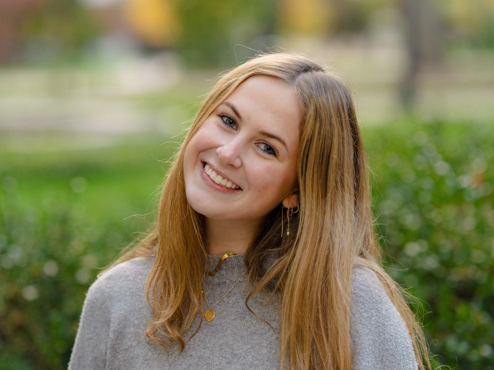 Gianna Martinelli wears a gray sweater while standing against an outdoor backdrop. 