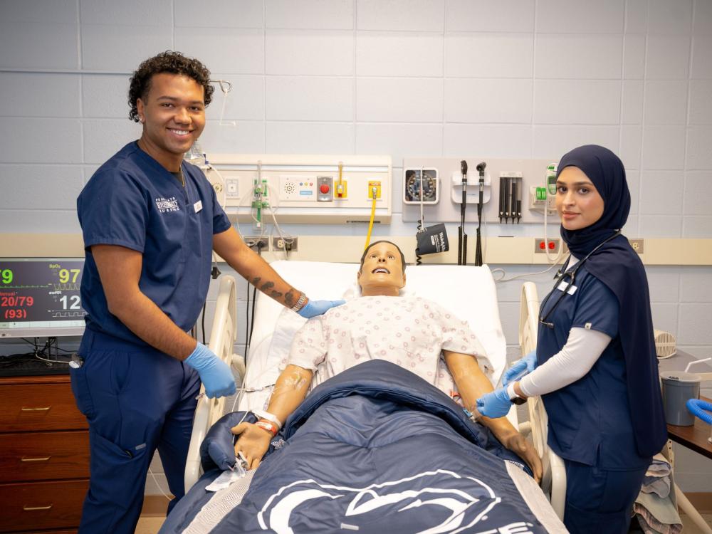 Two Penn State Behrend nursing students pose near a simulation mannikan.