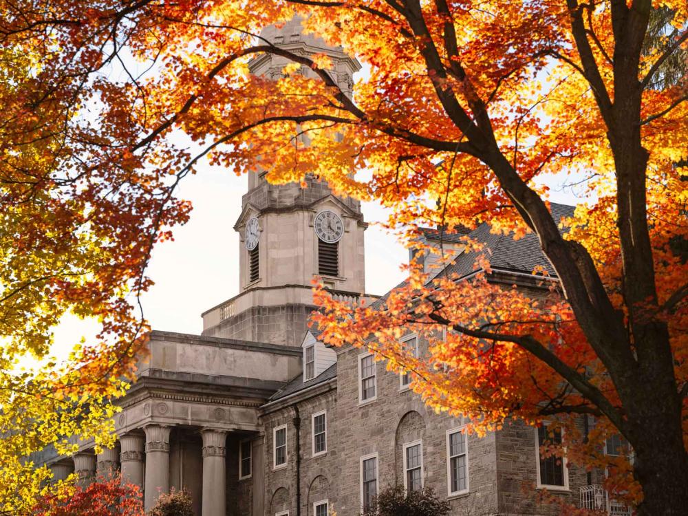 The tower of Old Main, partially blocked by trees with orange and red leaves.
