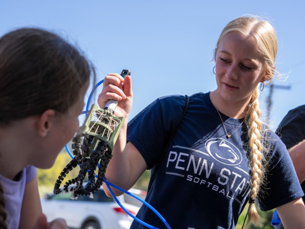A student holds up a robotic gripper for another student to see