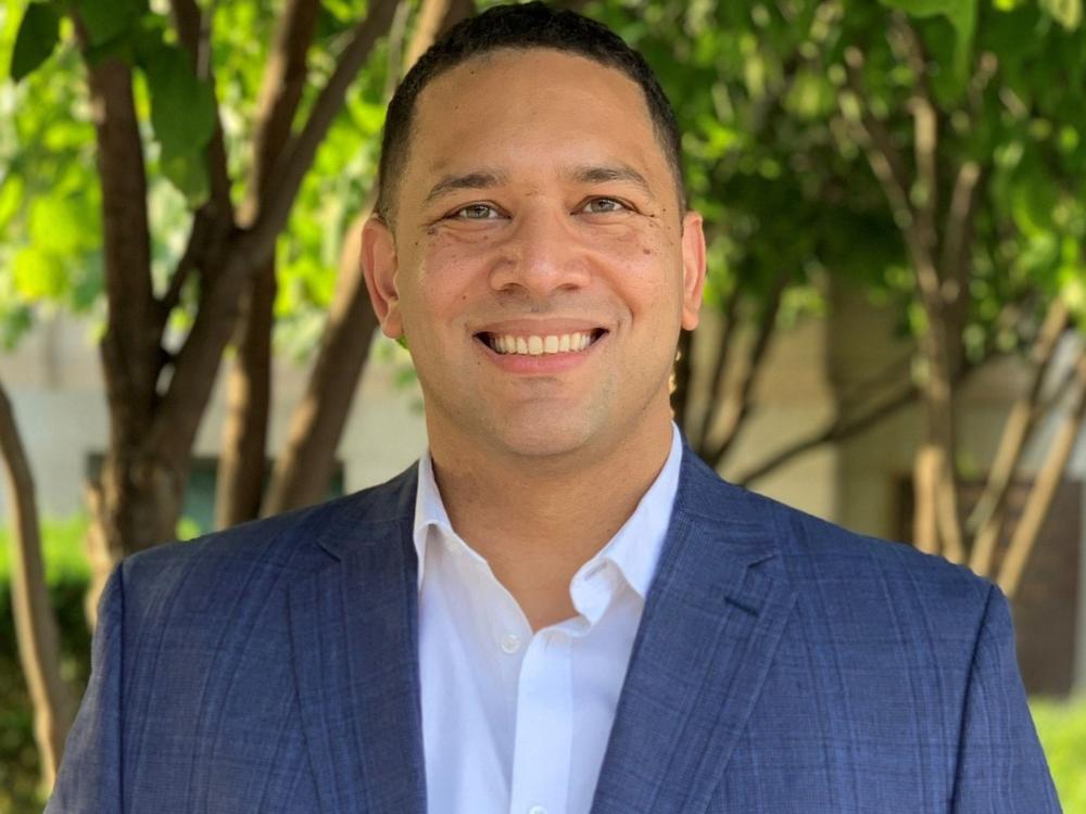 person with short dark hair, white unbuttoned dress shirt, gray suit jacket