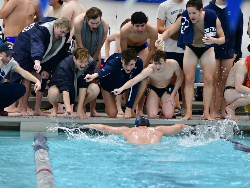 Members of the Penn State Behrend men's swimming and diving team cheer a teammate as he swims.