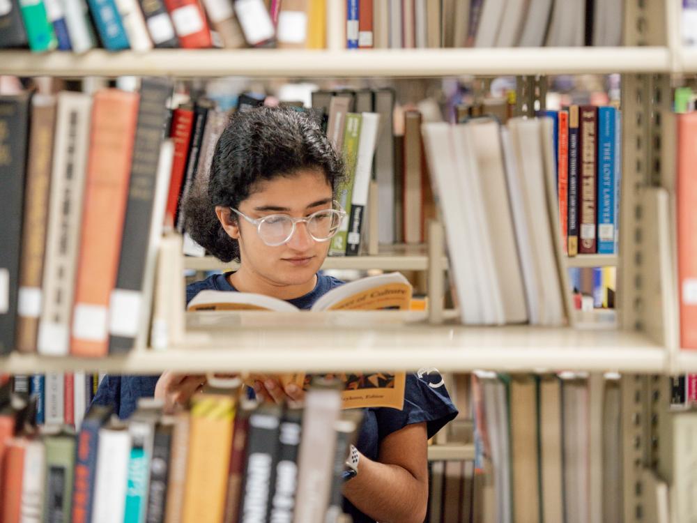 student seen through open bookshelf looking at book