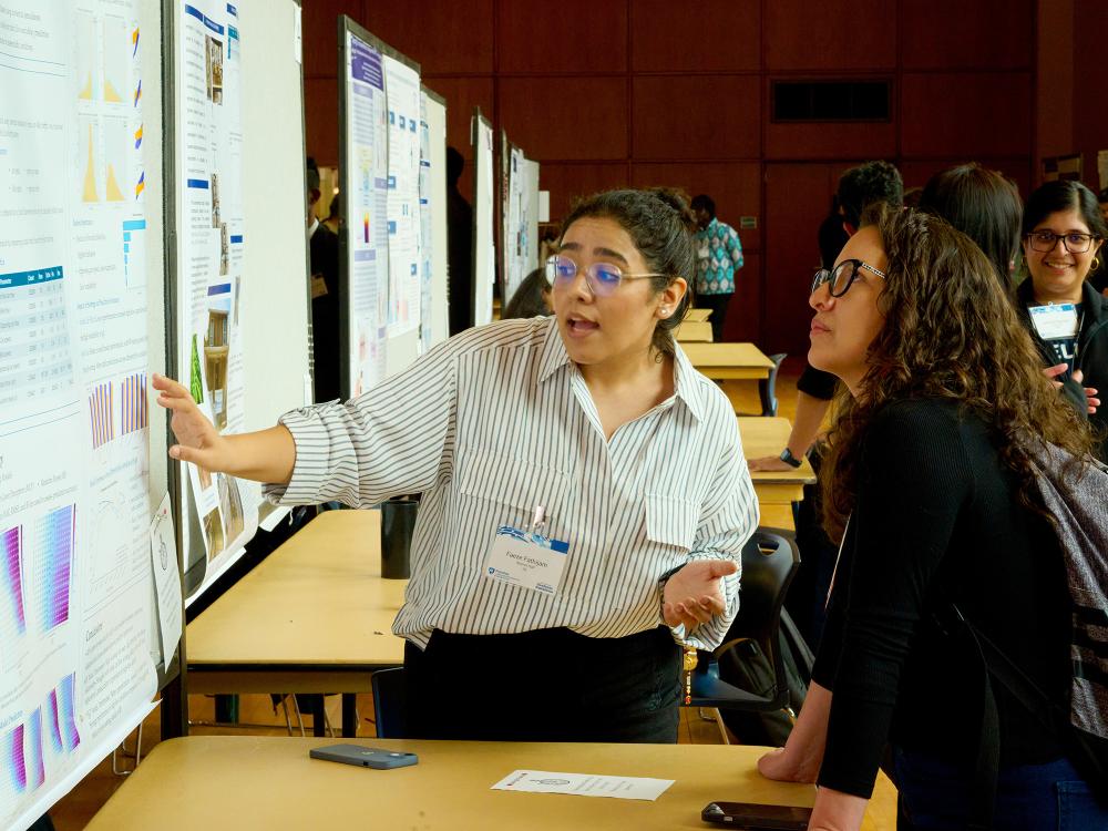Graduate student points to her poster while speaking with a judge at the 2025 Graduate Exhibition