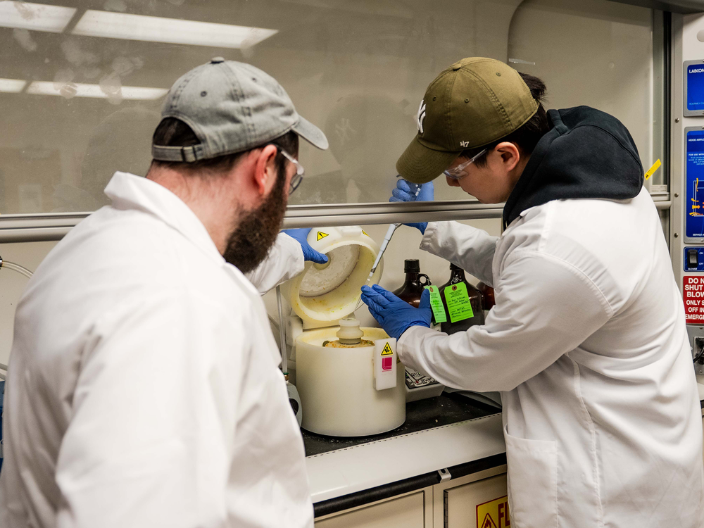 Dor Tillinger, doctoral candidate of mechanical engineering, and Donbae Lee, doctoral candidate of engineering science and mechanics, dressed in lab coats using lab equipment.