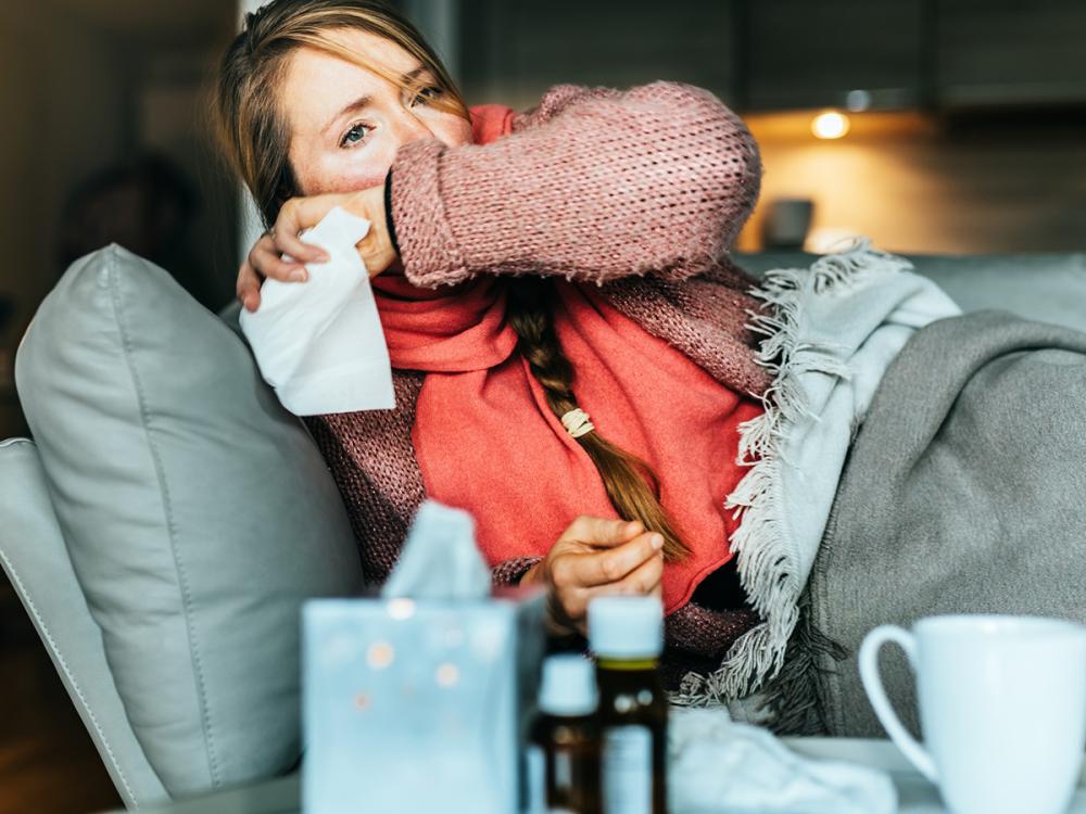 Woman coughing on a sofa and holding a tissue while sick with the flu.