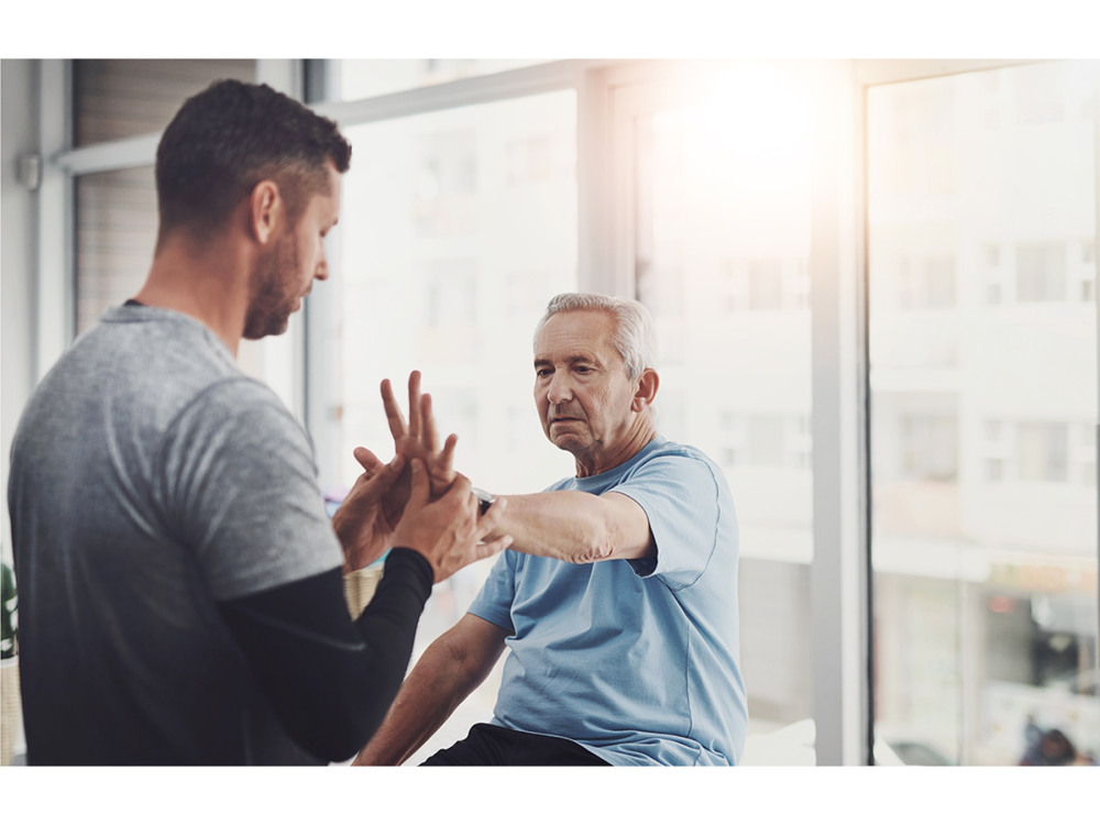 Older man doing hand therapy exercises with a physical therapist