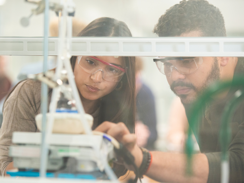 Two people wearing goggles observe something in a lab setting