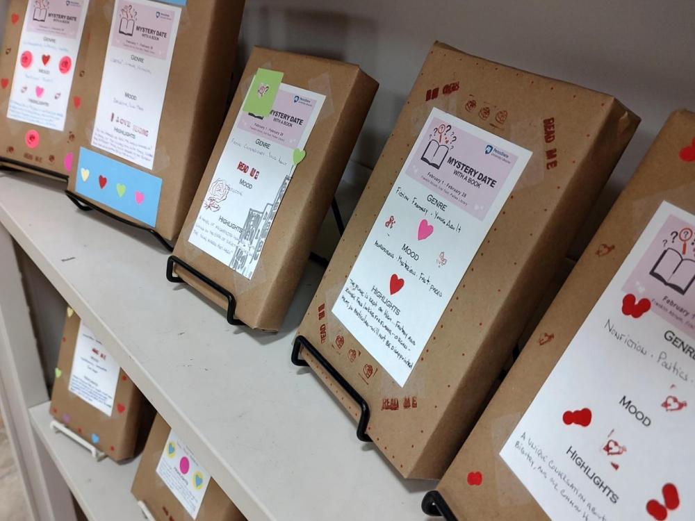 metal bookshelves lined with forward facing hardcover books wrapped in craft paper and decorated with stickers and written descriptions of stories within