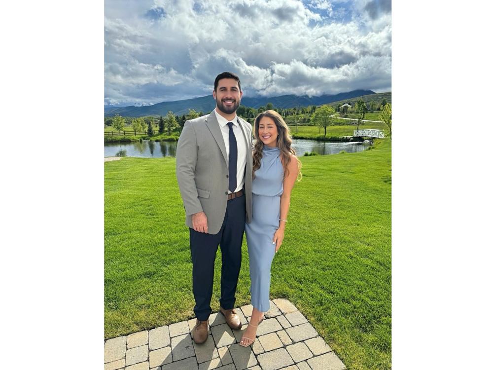 couple in formal attire on golf green with pond and bright sky in background