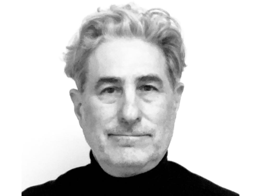 A black‑and‑white portrait of a person with short, wavy hair, wearing a dark top, shown against a plain white background.