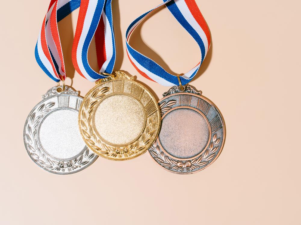 Three medals—gold, silver, and bronze—on red, white, and blue ribbons, arranged side by side on a light background.
