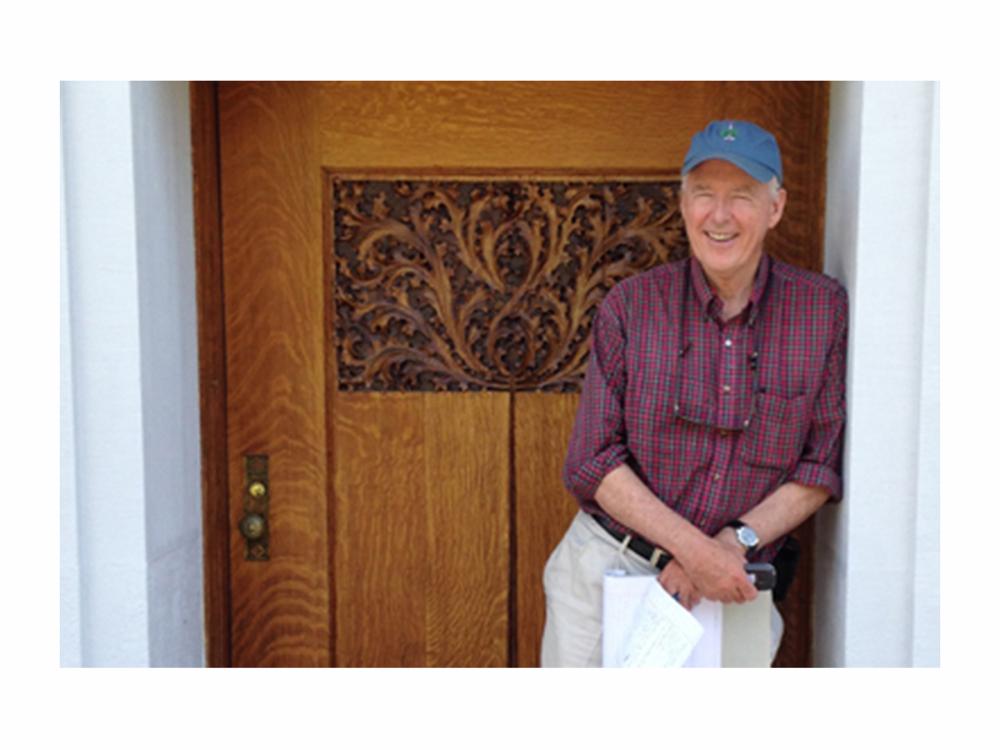Man in blue ballcap leans against a wall in front of a wooden door