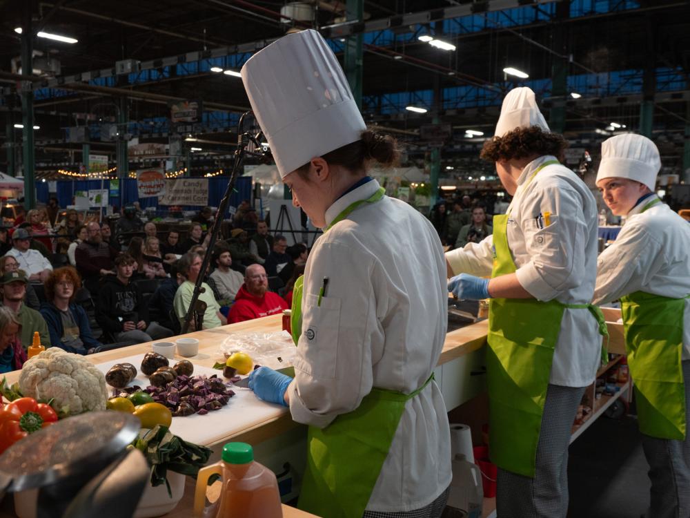 A line of chefs cook on a stage in front of an audience