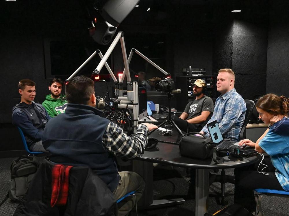 A group of people seated around a table with broadcast microphones.