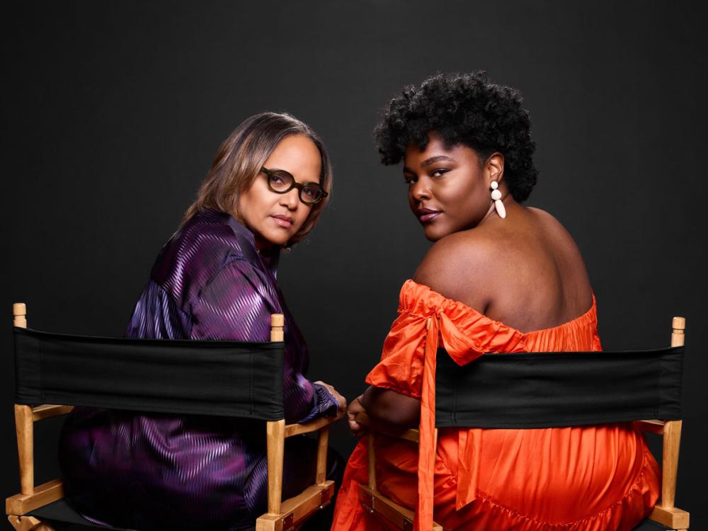 Two Black women sitting in director's chairs turn around to look at the camera.