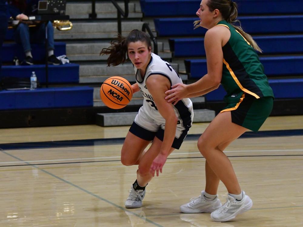 A member of the Penn State Behrend women's basketball team dribbles the ball past an opponent.