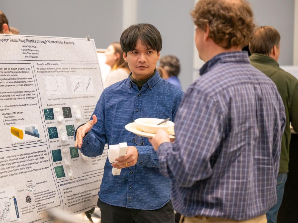 A researcher at Penn State Behrend discusses his work in front of a poster display.