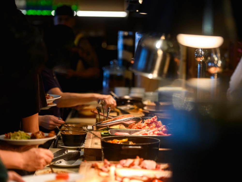 plates held over a long buffet with several types of meat and other foods