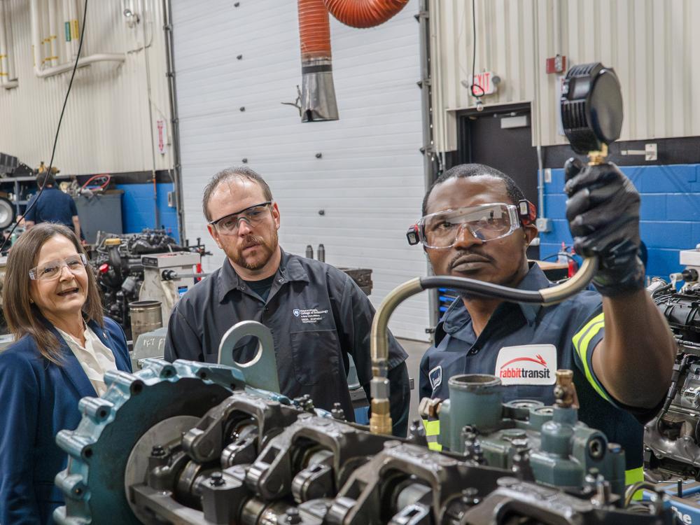 Several people watch someone else work on some equipment