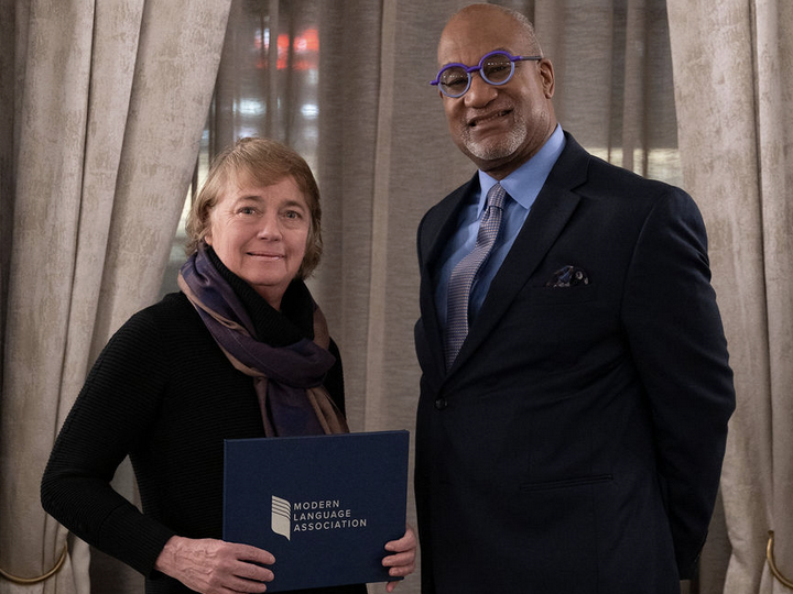 Celeste Kinginger wears a scarf and black outfit and holds certificate while standing next to Herman Beavers