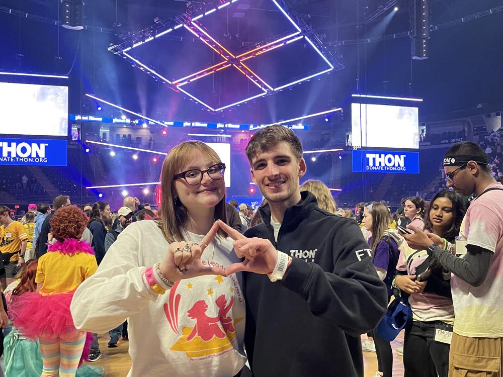 Two people pose in front of a stage inside an arena.