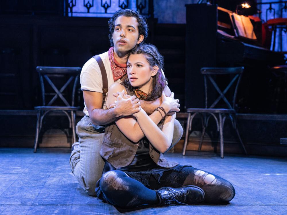 A man and woman sit on a stage in a loving embrace.