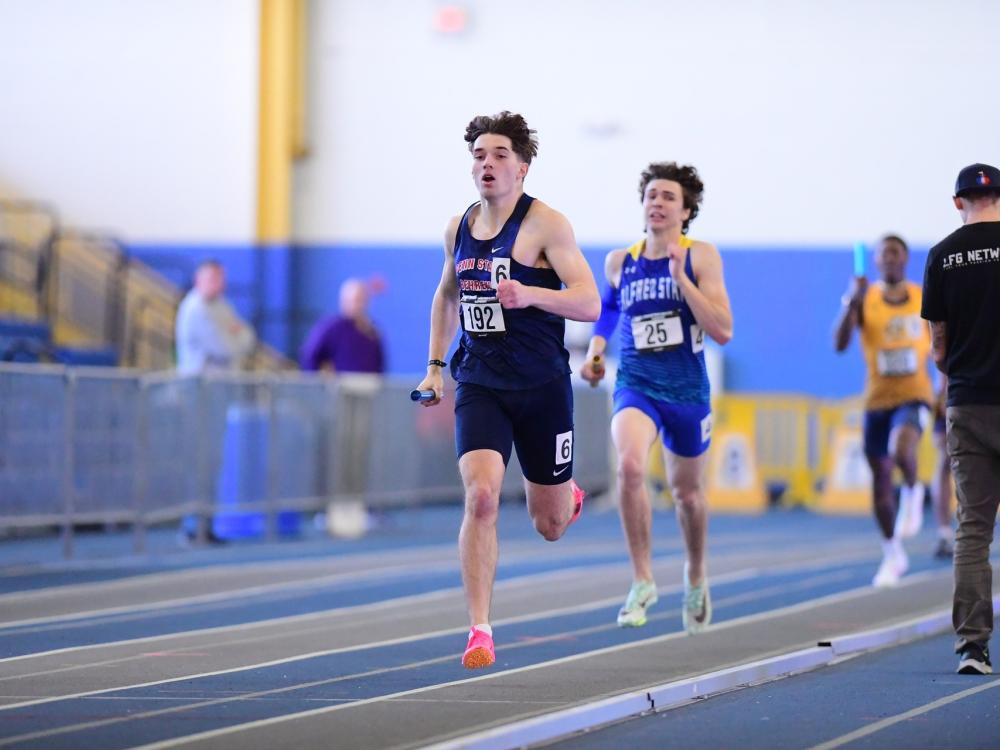 A member of the Penn State Behrend men's track and field team runs with the baton during a relay race.