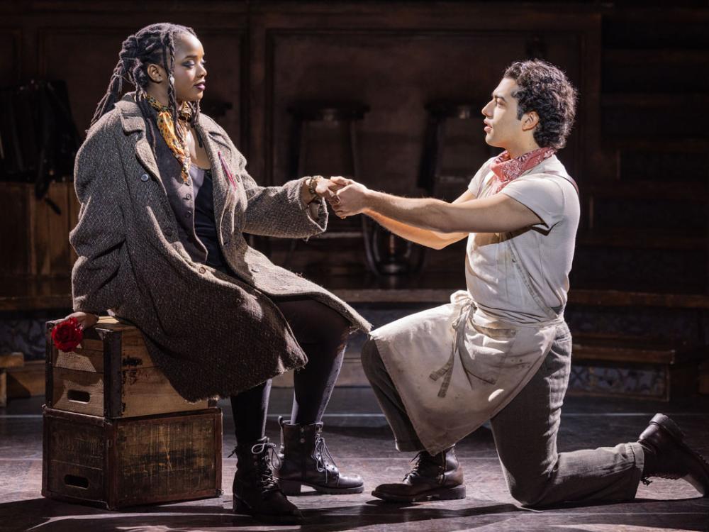 A man bends at the knee and holds the hand of a Black woman.
