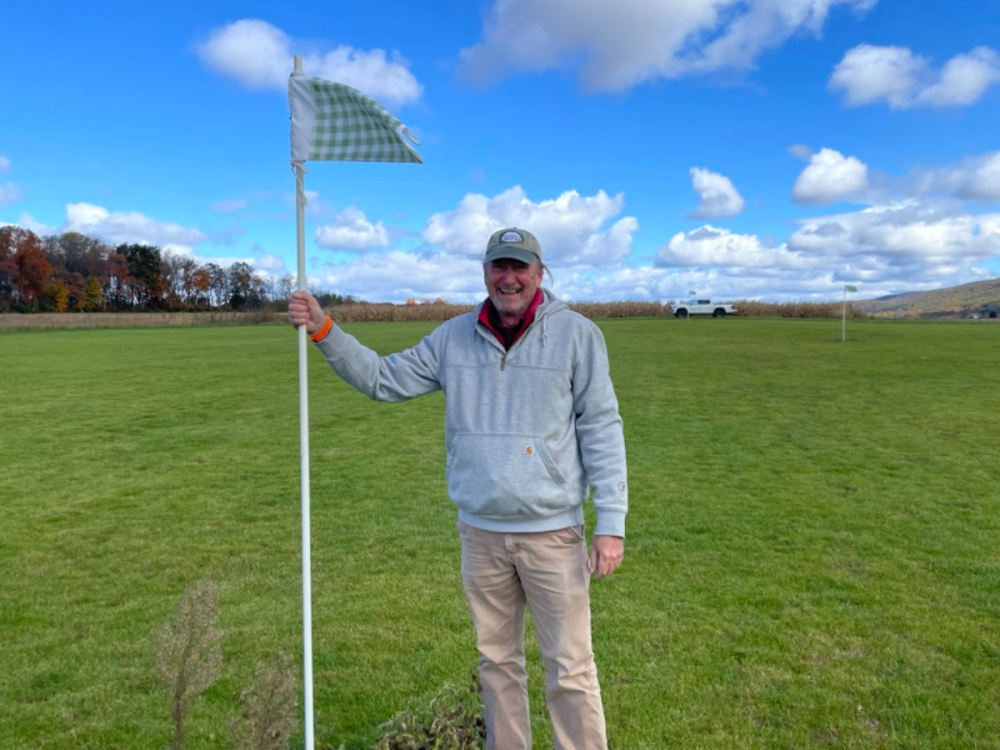 David Huff stands holding a golf flag on a golf course