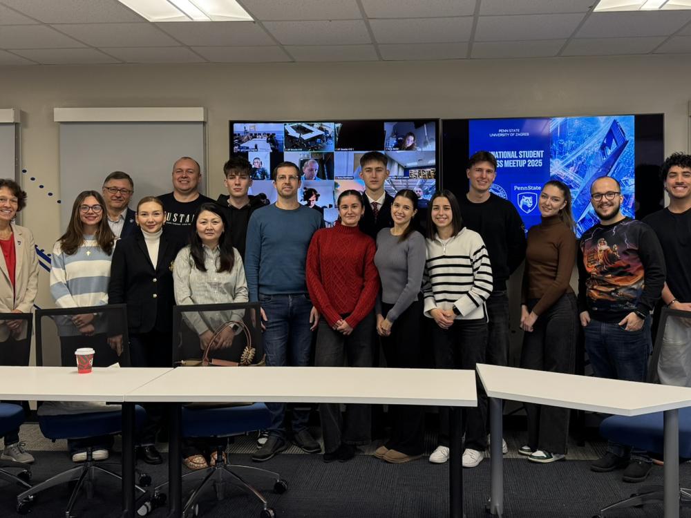 A group of students and faculty take a group photo in front a of a screen with Zoom call participants. 