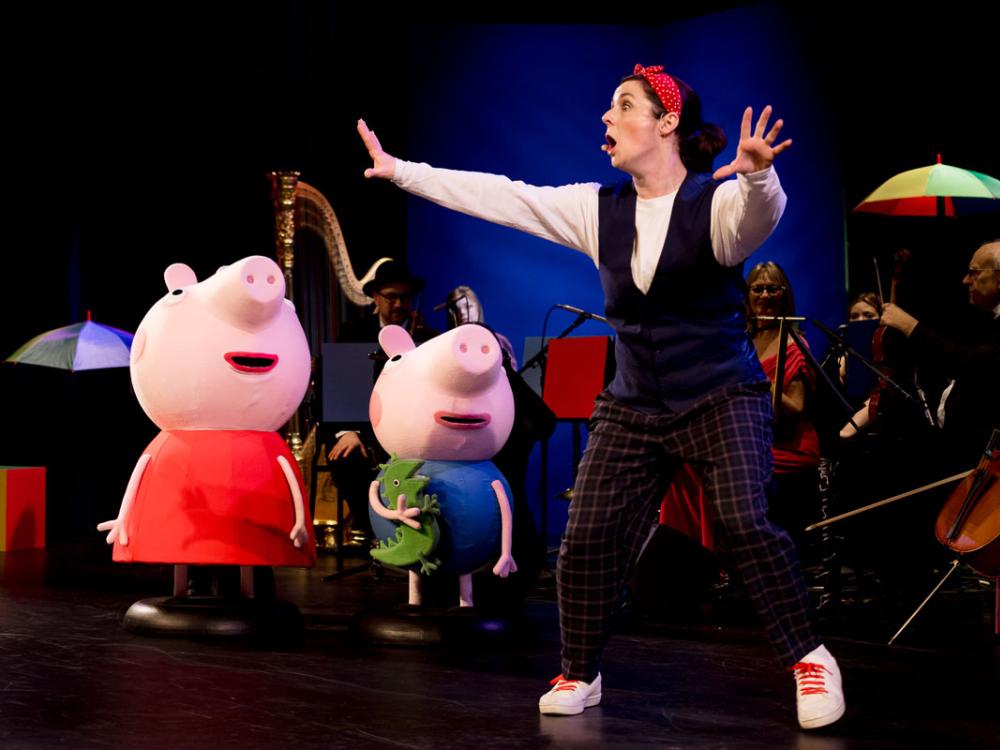 A woman reacts excitedly to something while standing next to pig puppets.
