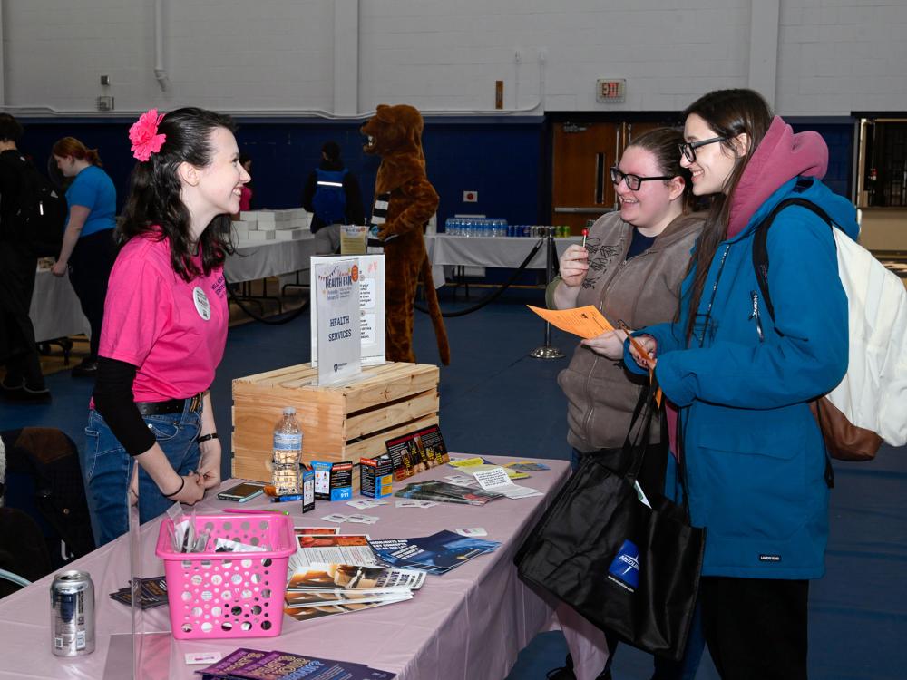 A student working at a table talks to two students