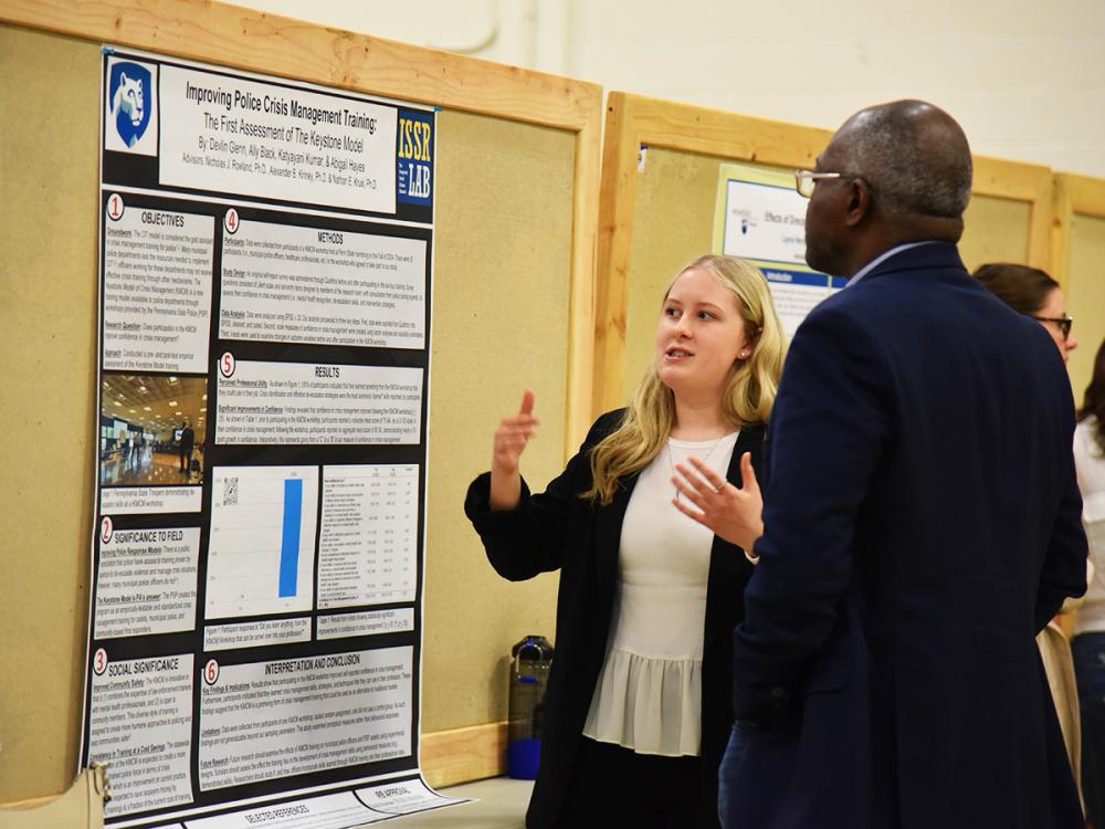 A student presenting a research poster and explaining findings to an attendee at an academic poster session.