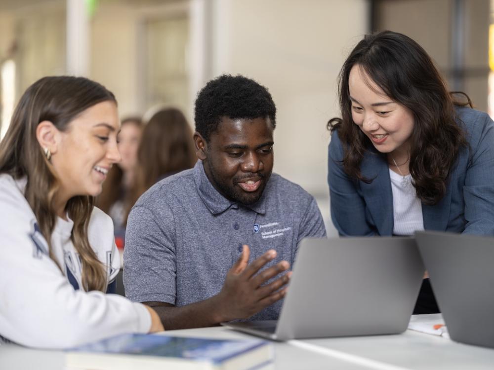 Two students and professor in the College of Health and Human Development work over a laptop.
