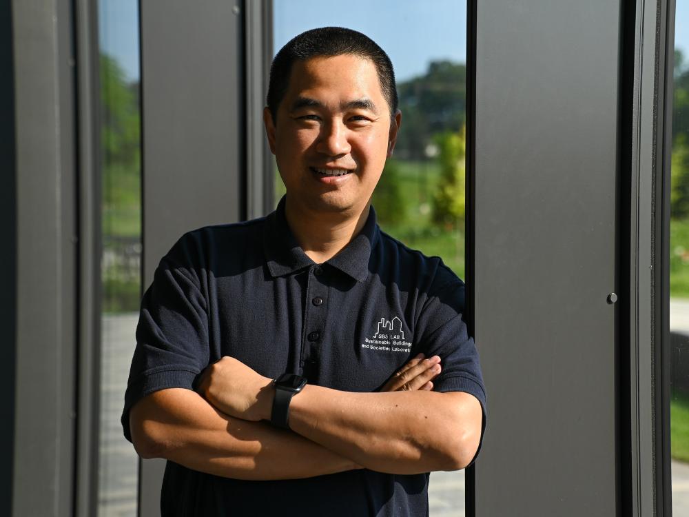 Wangda Zuo poses for a portrait with his arms crossed in front of a window.