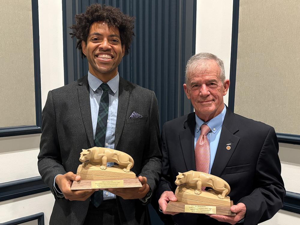 Two men standing side by side holding small statues