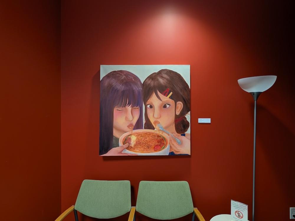 A painting of two girls eating hangs on a red wall.