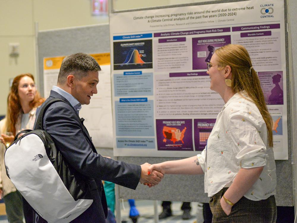 Man and woman shaking hands in front of a scientific poster