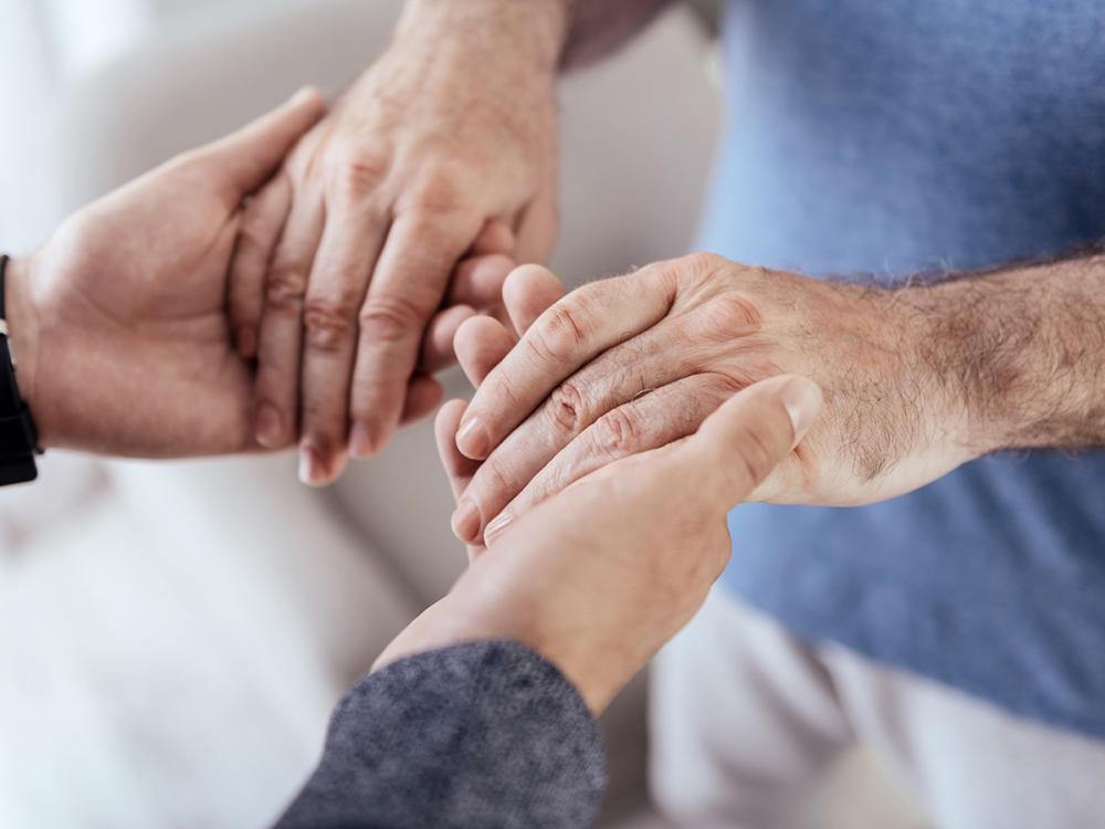 Several hands gently hold and support one another, symbolizing care, compassion, and human connection.