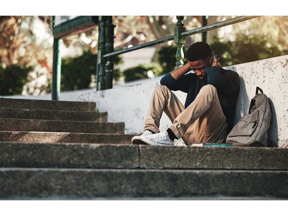 Young man with head bowed and sitting against a staircase.
