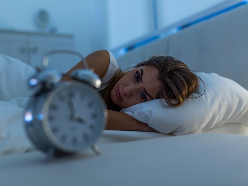 Woman with insomnia lying in bed looking at alarm clock.