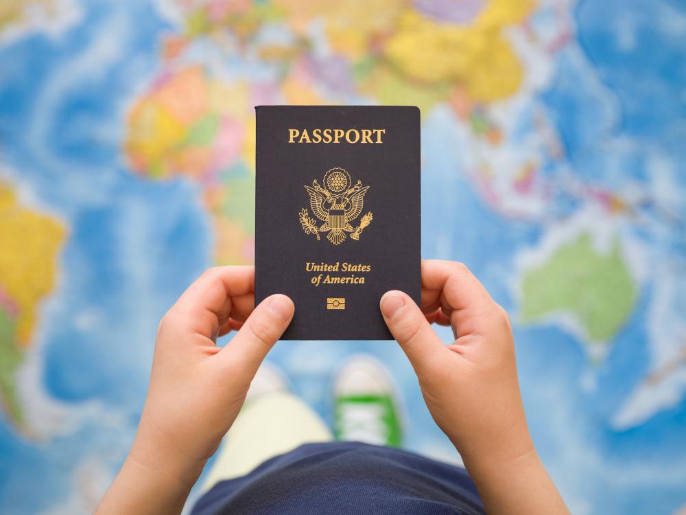 A child's hands holding a U.S. passport, with a map of the world in the background