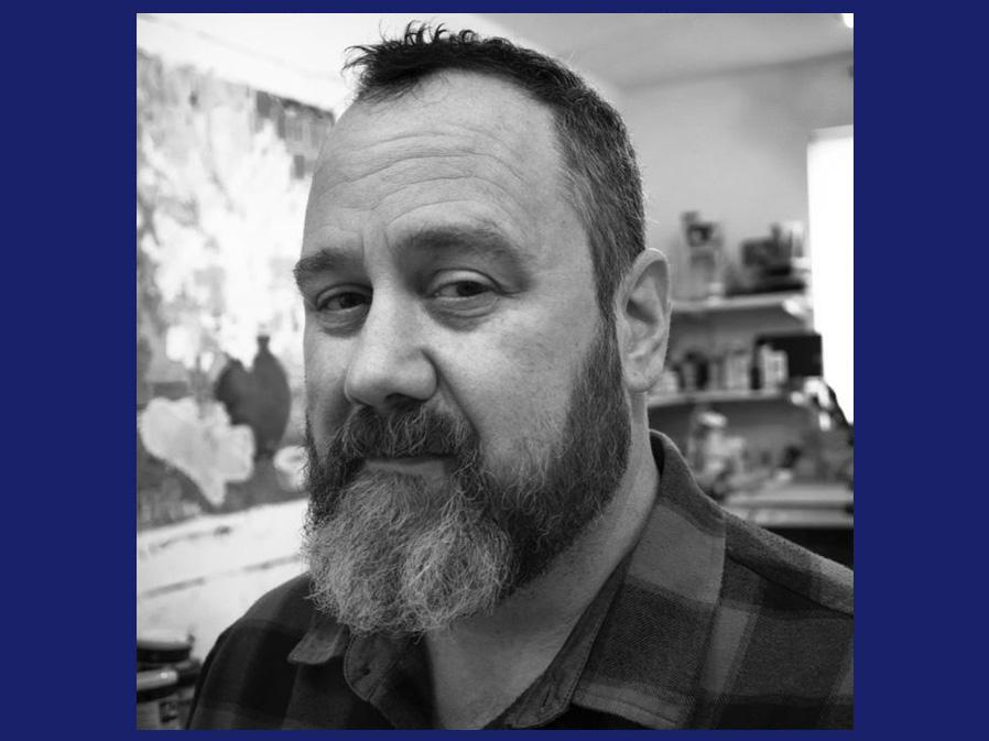 A black and white head shot of a white man with short hair and a beard